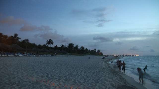 Ein breiter Sandstrand mit Palmen. Junge und alte Menschen genießen die letzten Sonnenstrahlen am Meer in Varadero.